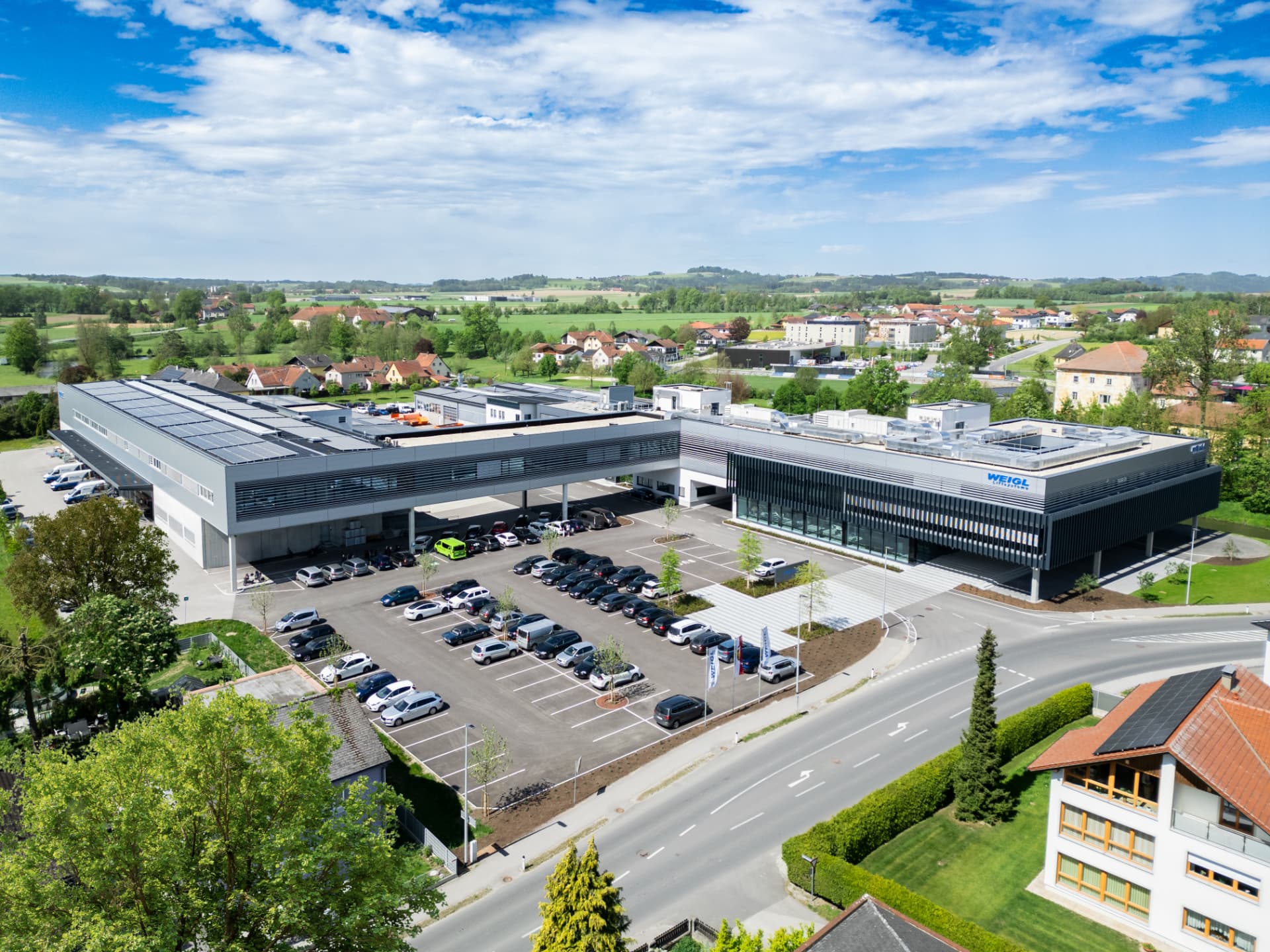 Luftaufnahme des WEIGL Firmengebäudes mit Parkplatz und Photovoltaikdächern