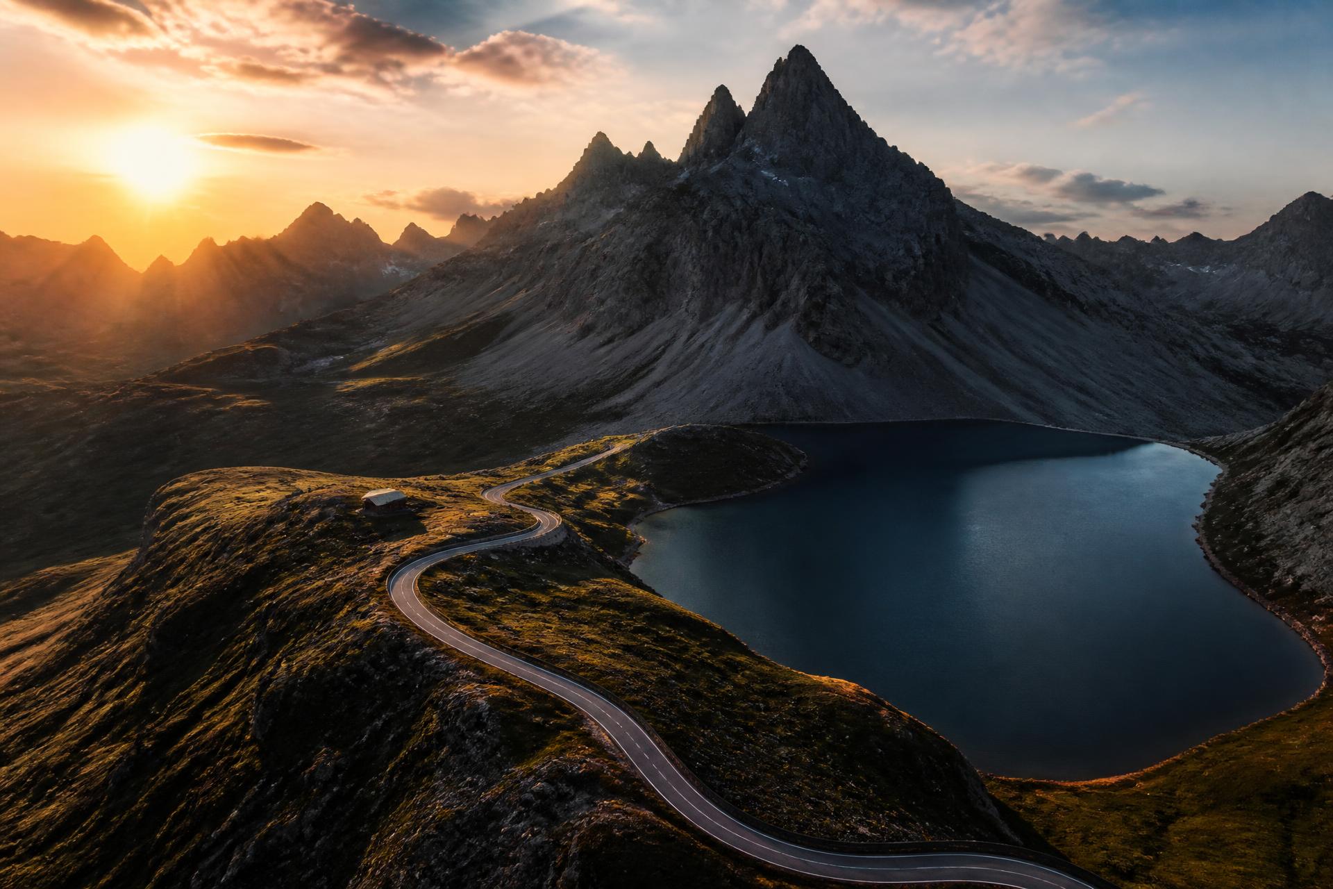 Luftaufnahme einer Passstraße an einem Bergsee im Abendlicht